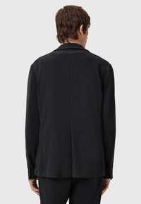 Black blazer, structured fabric, single vent at the back, classic lapel collar, two-button closure, fitted sleeves with button accents.