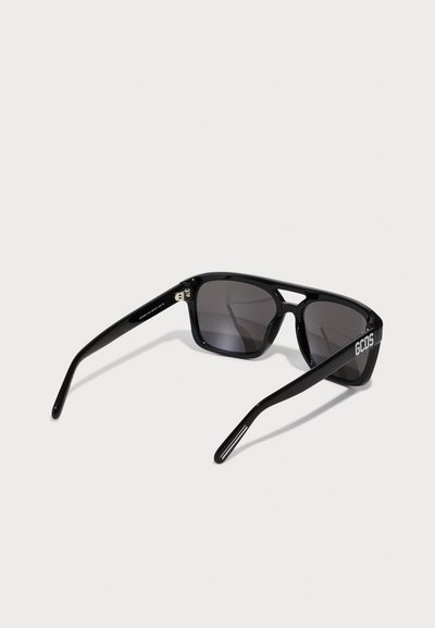 Gafas de sol negras con montura rectangular, lentes oscuros y un acabado brillante. Logo "GCDS" impreso en el lateral. Diseño elegante y brazos resistentes.
