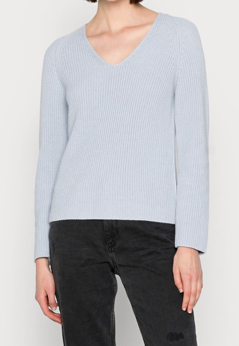 Ljusblå stickad tröja med V-ringning och långa ärmar, med ribbat mönster. Matchas med svarta byxor.