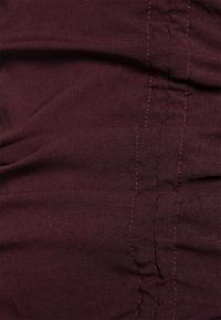 Burgundy tyg med horisontella veck och kontrasterande rosa sytråd. Mjuk textur med en slät yta som visar en jämn färgdjup.