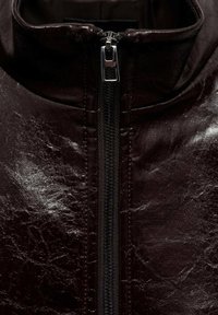 Dark brown leather jacket with a high collar and front zipper. Surface has a glossy texture with subtle creases, enhancing its rugged appearance.