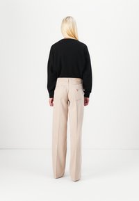 Světle béžové kalhoty s širokými nohavicemi a vysokým pasem, v kombinaci s černou mikinou. Viditelné šití a minimalistický design. Pohled zezadu.
