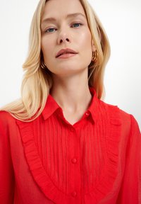 Rote, durchsichtige Bluse mit gerafftem Kragen, Knopfverschluss und vertikalen Falten. Flach, weiche Textur mit leichtem Aussehen.