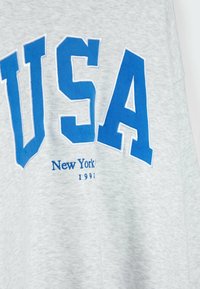 Tissu gris avec le texte "USA" en grand en bleu et en dessous, en plus petit bleu, "New York 1991".