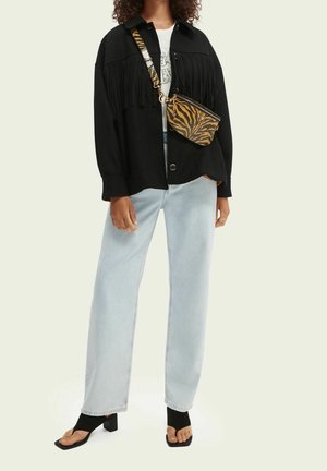 Zwarte jack met franjes, wit T-shirt met print, lichtblauwe losse spijkerbroek en zwarte sandalen. Accessoire: een kleine zwart-oranje tas met tijgerprint.