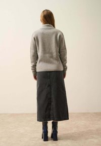 Jersey de lana gris con un cuello alto, combinado con una falda larga de mezclilla negra. El calzado cuenta con botines de tacón azul.