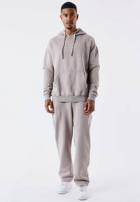 Lichtgrijze hoodie met een voorzak, capuchon met trekkoord en bijpassende sweats. Kenmerken zijn een ontspannen pasvorm en zachte textuur, gecombineerd met witte schoenen.