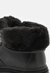 Botte noire en cuir avec un col en fourrure noire douce, une surface texturée et des coutures renforcées le long de la semelle.