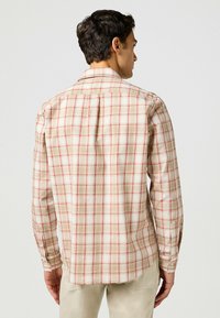 Camisa a cuadros beige con patrón de tartán rojo y blanco. Mangas largas, puños con botones y detalle en el yugo trasero. Material de algodón, corte relajado.