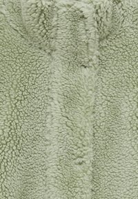 Lys grøn fleece stof med en blød, tekstureret overflade, der har et fluffy udseende og subtile variationer i tykkelsen.