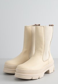 Stivaletti color crema realizzati in pelle liscia, con pannelli laterali elastici e suole in gomma spessa e texture per una maggiore trazione.
