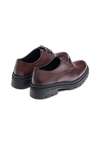 Zapatos de piel marrón con cordones, punta redonda, suela de goma negra de perfil bajo y detalles cosidos cerca del talón.