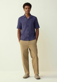 Short-sleeve navy button-up shirt with a textured pattern, paired with light beige loose-fitting pants and gray slip-on shoes.