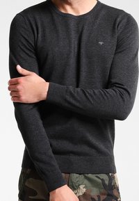 Dark grey sweater made of soft fabric, featuring a crew neckline, long sleeves, and ribbed cuffs. Small logo on the chest.