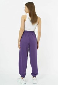 Lila Jogginghosen mit einem elastischen Bund, gerippten Knöcheln und einer lockeren Passform, kombiniert mit einem weißen ärmellosen Oberteil und weißen Turnschuhen.