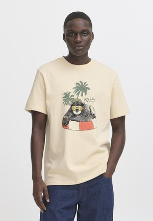 Beige katoenen T-shirt met een graphic van een kat in een zonnebril op een reddingsboei met palmbomen. Korte mouwen en een ronde hals.