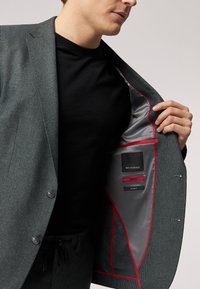 Blazer grigio testurizzato con un design aderente. L'interno presenta una fodera grigia con dettagli rossi e etichette: "ROY ROSSON", "Slim Fit" e "Stretch".