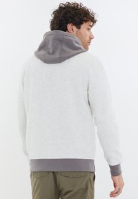 Felpa grigia chiara con cappuccio e polsini grigio scuro. Tessuto morbido, vestibilità rilassata e coulisse regolabile sul cappuccio.