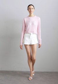 Light pink sweater with "IT AND GODS" in silver lettering, paired with a white pleated mini skirt and white strappy sandals.