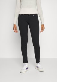 Jeans slim fit negros con una textura suave, que cuentan con bolsillos frontales y cierre de botón metálico. Combinados con zapatillas blancas con acentos morados.