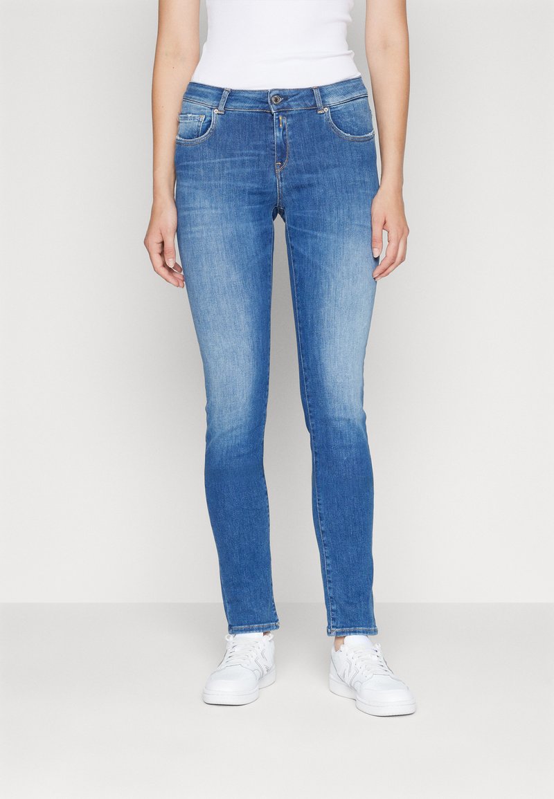 Jeans skinny bleus avec un design délavé, cinq poches, fermeture à bouton et une texture denim lisse, assortis à des baskets blanches.