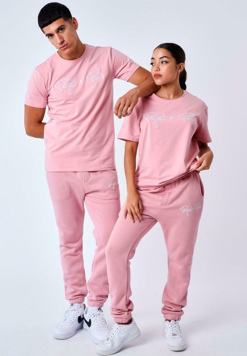 Dos modelos llevan sudaderas y joggers de algodón de color rosa claro a juego, con un estampado blanco del logo "Project x Paris" en la parte frontal.