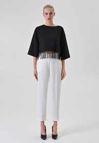 Top corto nero con dettagli in pizzo a frange sull'orlo, abbinato a pantaloni bianchi sartoriali e tacchi a spillo neri. Tessuto dalla texture liscia.