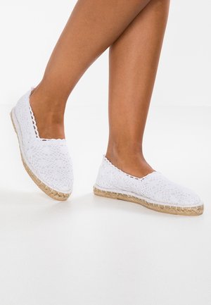Espadrilles en dentelle blanche avec une semelle en jute tissée et des détails cousus, présentant un design ouvert et une construction plate.