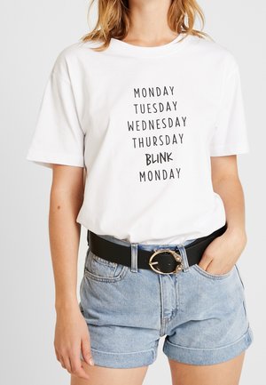 White cotton t-shirt features black printed text listing days of the week, with "BLINK" emphasized. Paired with denim shorts and a black belt.