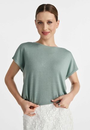 Jasnozielona bluzka z krótkim rękawem, wykonana z miękkiego, teksturowanego materiału. Luźny krój ma okrągły dekolt i jest zestawiony z białą spódnicą w kwiatowy wzór.