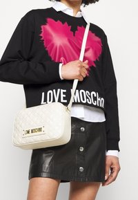 Schwarzer Sweatshirt mit pinkem Herz-Graphic und "LOVE MOSCHINO"-Text, kombiniert mit einem schwarzen Lederrock und einer cremefarbenen gesteppten Umhängetasche.
