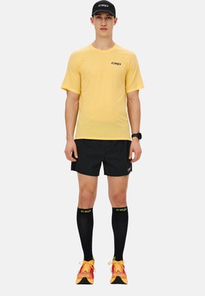 Yellow short-sleeved running shirt with a textured pattern, paired with black shorts, knee-high black compression socks, and colorful running shoes.