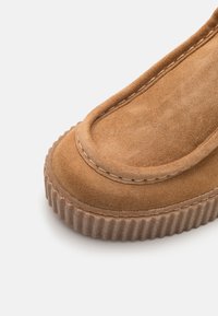 Mockasiner i ljusbrunt suede med en rund tå. Har kontrasterande sömmar och en texturerad, ribbad gummisula.