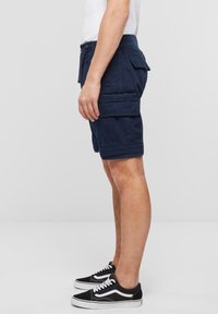 Pantaloni scurți cargo în nuanța bleumarin, cu multiple buzunare, talie cu bucle pentru curea și o croială lejeră. Asortați cu pantofi sport negri și albi.