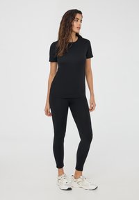 Czarna krótki rękaw t-shirt i legginsy, wykonane z elastycznej tkaniny, dopasowany krój, gładka tekstura, połączone z białymi sportowymi trampkami.