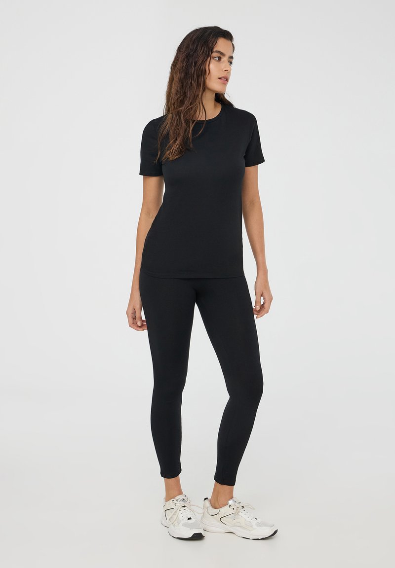 Czarna krótki rękaw t-shirt i legginsy, wykonane z elastycznej tkaniny, dopasowany krój, gładka tekstura, połączone z białymi sportowymi trampkami.