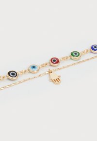 Bracelet plaqué or ornée de charms en émail représentant des yeux malins colorés et d'un pendentif en forme de main, avec un design de chaîne délicate.