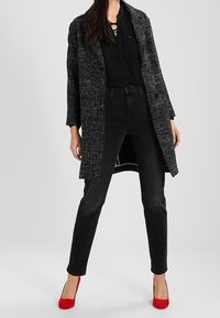 Textured black and white tweed coat over a black top and fitted black jeans, complemented by bright red high heels.