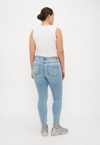 Light blue skinny jeans made of denim, featuring a mid-rise waist, back pockets, and a textured fabric. Paired with a white sleeveless top.