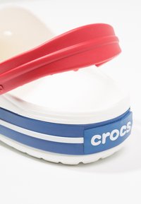 Sandália plataforma vermelha e azul com detalhes brancos, feita de plástico durável. Apresenta uma sola espessa e um logótipo em relevo na lateral.