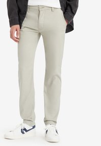 Jasnoszare bawełniane spodnie o prostym kroju, z guzikiem z przodu i subtelnym przeszyciem po bokach, zestawione z białymi trampkami.