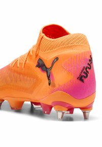 Scarpa da calcio arancione con tomaia sintetica testurizzata, accenti neri del logo e un tallone sfumato rosa. Presenta un colletto simile a una calza e quattro tacchetti.