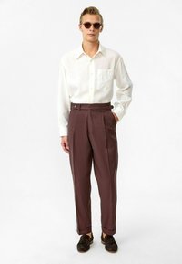 Witte lange mouwen shirt, met pocketdetail, gecombineerd met hoge taille donkerbruine broek, voorzien van riemlussen en decoratieve knopen. Semi-omrand zonnebril.