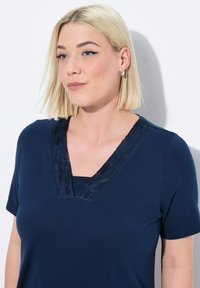 T-shirt a V nero con maniche corte, caratterizzato da un bordo in satin texturizzato lungo il collo per un tocco di dettaglio. Realizzato in morbido cotone.