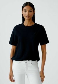 Zwarte katoenen t-shirt met korte mouwen en een ronde halslijn, voorzien van een subtiele logo op de borst. Gecombineerd met witte jeans.