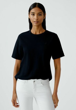 Zwarte katoenen t-shirt met korte mouwen en een ronde halslijn, voorzien van een subtiele logo op de borst. Gecombineerd met witte jeans.