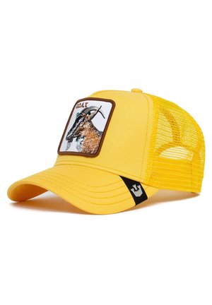 Gorra de camionero amarilla con un parche bordado en marrón y blanco que presenta un diseño de cabra. Parte trasera de malla y visera curvada. Acento negro en el lado.