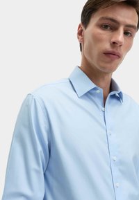 Jasnoniebieska koszula z długim rękawem, z kołnierzykiem rozłożonym, gładką fakturą materiału i białymi guzikami, o dopasowanym kroju.