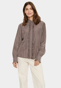 Långärmad blus i dämpad taupe, med rynkad framplacket och draperade ärmslut, tillverkad av mjukt, lätt material.