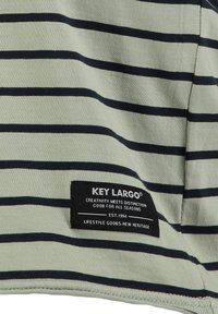 Tela a rayas verdes con líneas horizontales en azul marino oscuro. Incluye una etiqueta negra con texto en blanco, que indica la marca y la información.